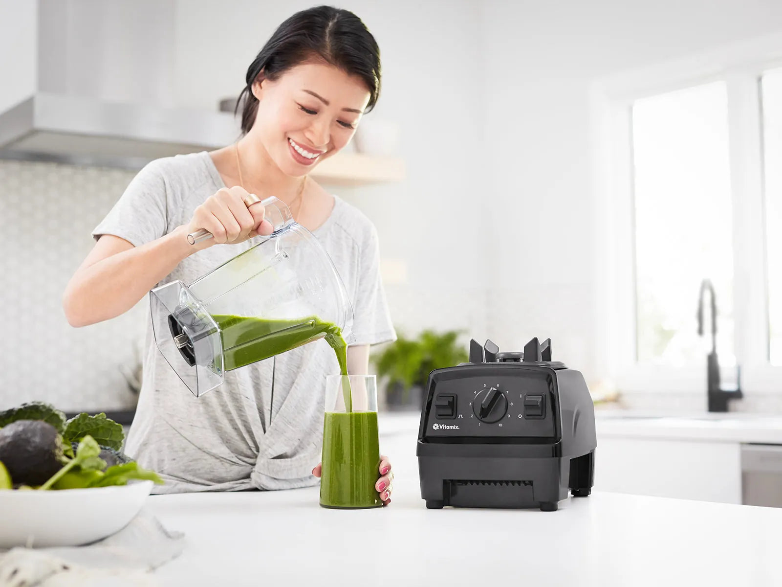 Pouring a green smoothie from a Vitamix jug, a Vitamix Explorian E310 on the bench