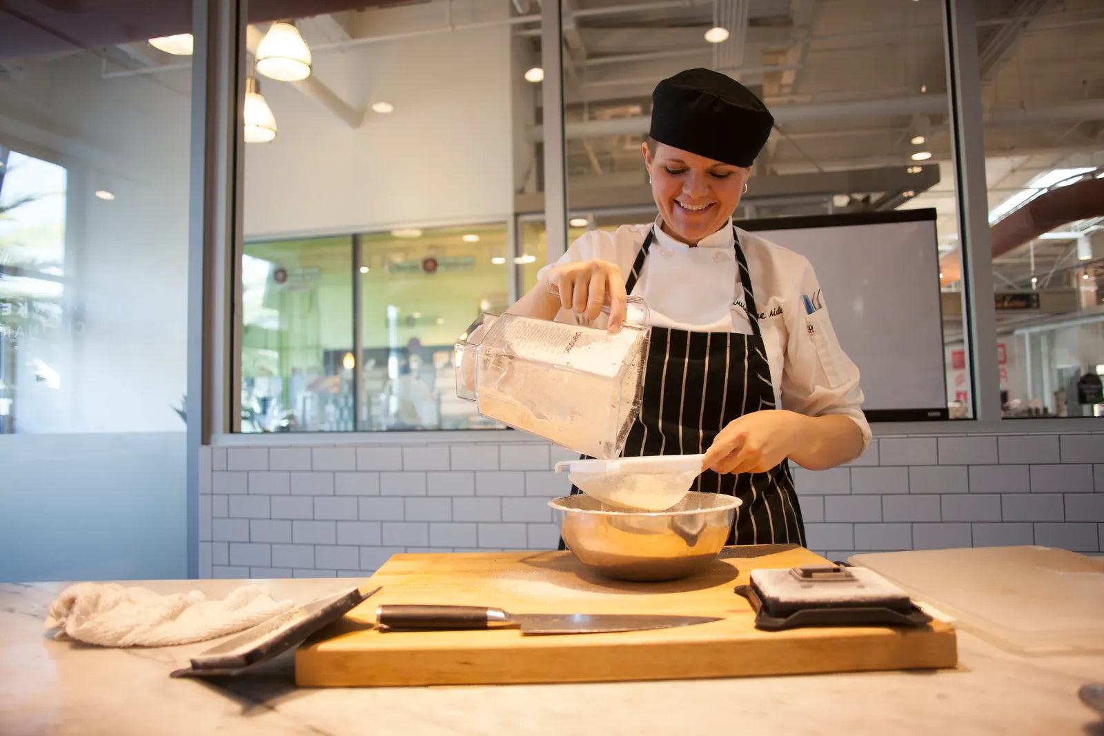A smiling chef pouring a blend from a Blendtec jar through a sieve in a busy kitchen