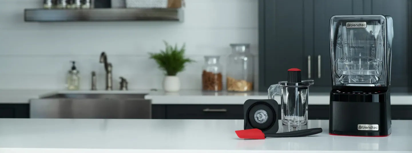 A Blendtec Professional 800 blender with its sound cover on a white bench in a modern kitchen