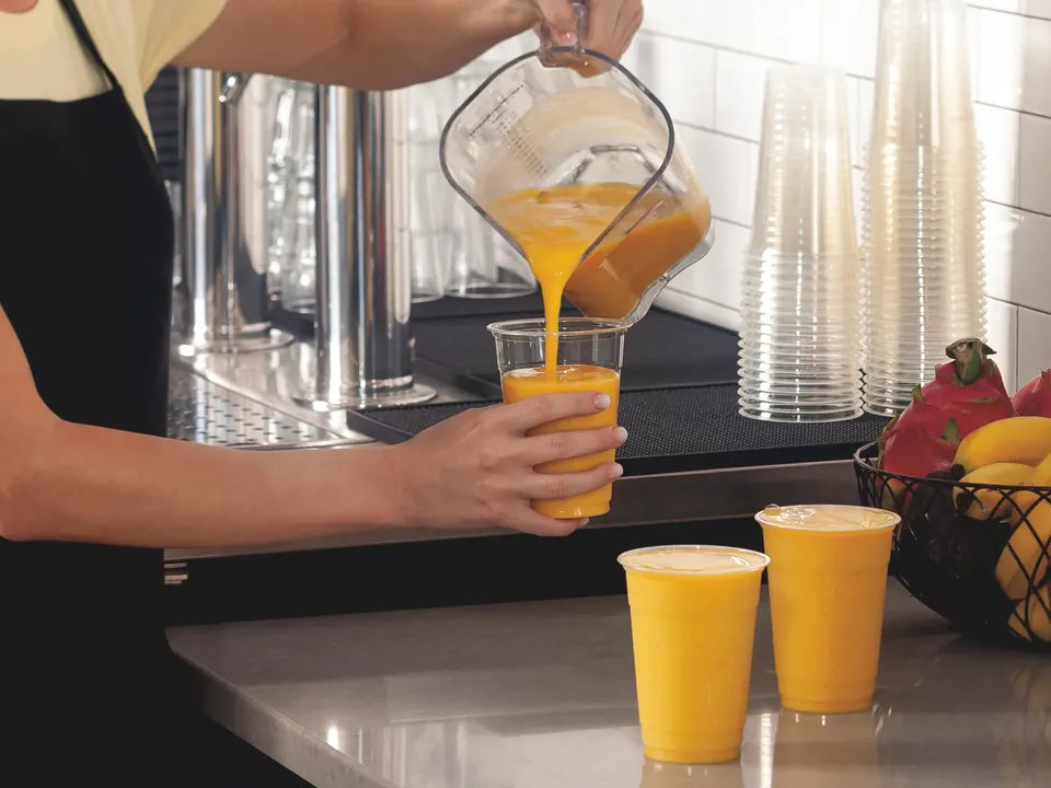 Pouring mango smoothies from a blender jug at a cafe bench