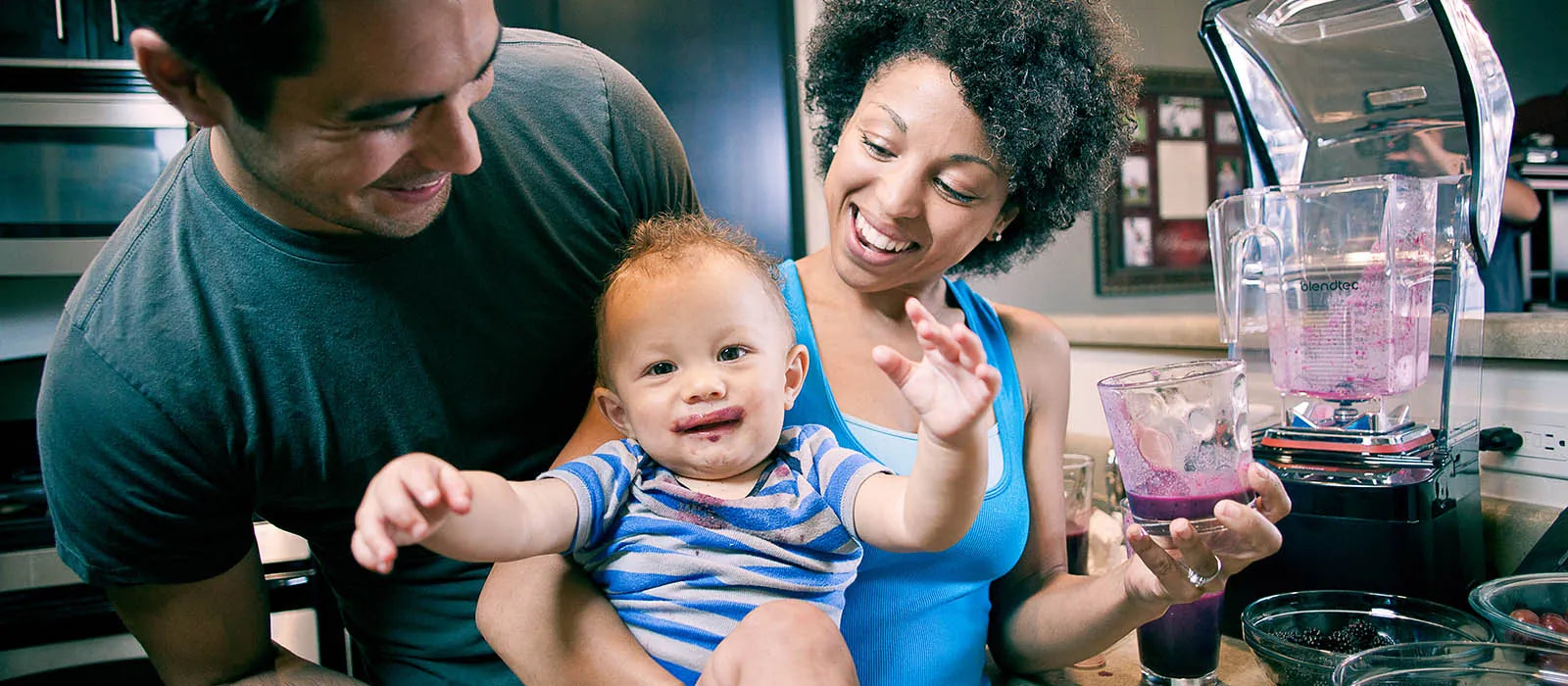 A father, a mother and their baby sharing a berry smoothie beside a Blendtec blender
