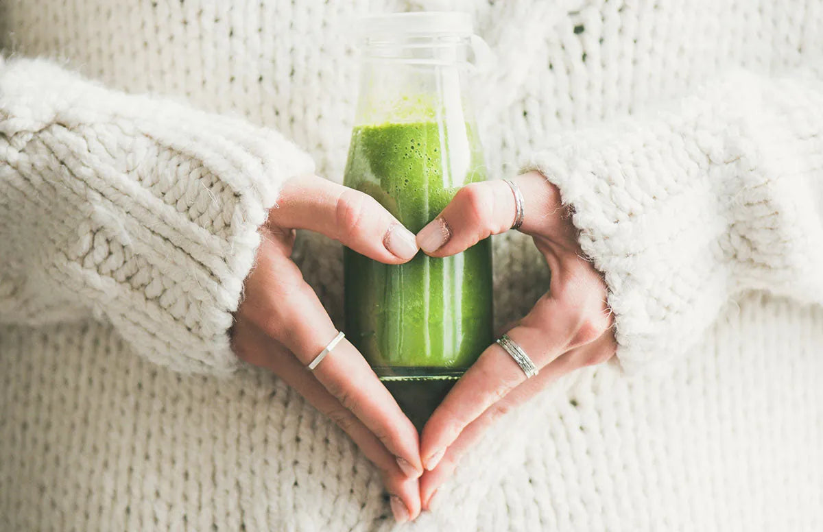 Two hands making a heart shape around a bottle of green smoothie